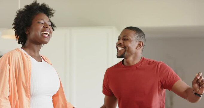 African American couple sharing shy glance sparking playful fist pump and dancing near fridge