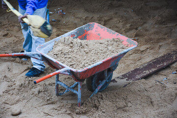 Wheelbarrow next to pile of sand on concrete surface