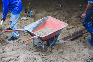 Wheelbarrow next to pile of sand on concrete surface