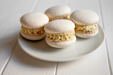 Macarons with crisp shells and creamy yellow poppy seed filling, artfully arranged on a white ceramic plate over a clean wooden tabletop, minimal dessert still life
