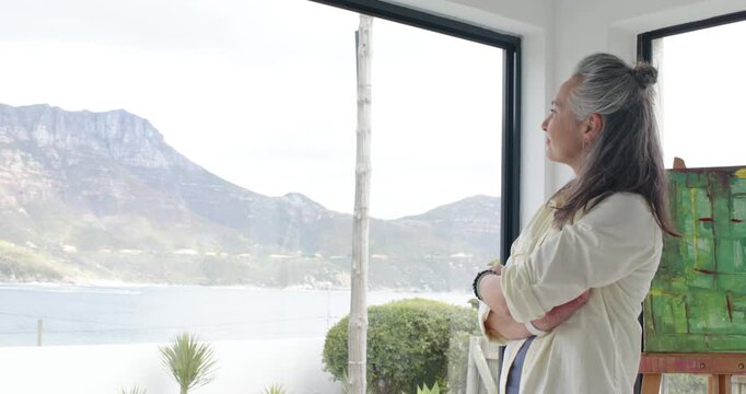 Entering senior woman smoothing hair and bracelets seeking inspiration by canvas, copy space