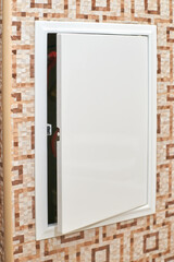 Open electrical panel on tiled wall with geometric pattern showing interior wiring and cables.