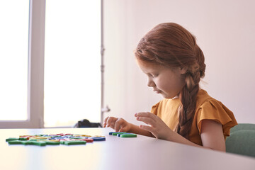 Young caucasian girl playing with colorful letters at table in bright room.