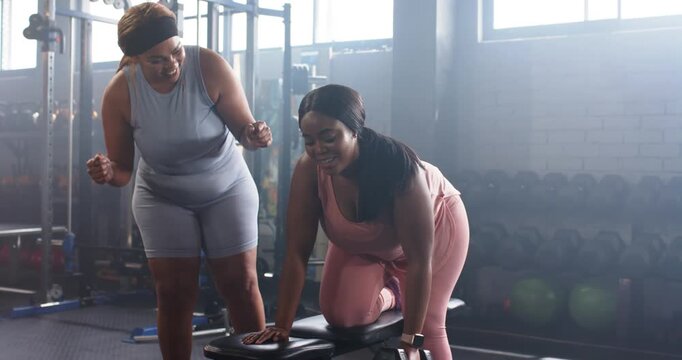 Female coach cueing trainee rowing dumbbell for tone on gym bench, high five checking watch