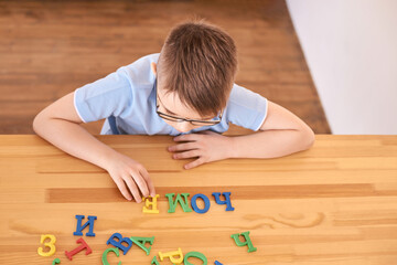 Caucasian male child playing with colorful alphabet letters on wooden table.
