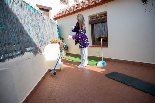 Teenage girl taking responsibility at home by sweeping outdoor patio on a sunny day, contributing to house chores in a calm environment and promoting domestic collaboration
