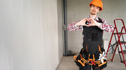 Builder, foreman, repairman wearing tool belt hard hat and overalls at construction site showing...