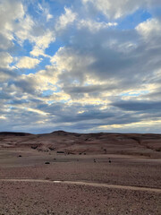 Cloudy evening sky above the vast rocky Moroccan desert, soft light over rolling barren hills and scattered shrubs