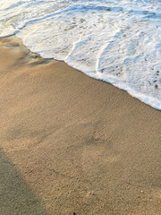 Gentle wave washing the smooth sandy beach, soft foam patterns on wet sand background, closeup view from above