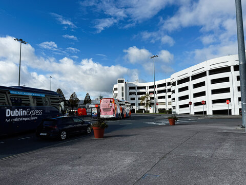 Busy Dublin bus station scene in Ireland with DublinExpress buses beside a modern parking garage under a blue sky