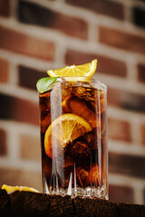 Cuba Libre in a glass with brown rum, cola, mint and lemon on brick background. Cuba Libre or long...