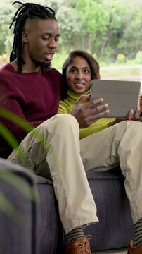 Vertical video: Holding tablet, couple scrolling content on patio sofa for coffee break