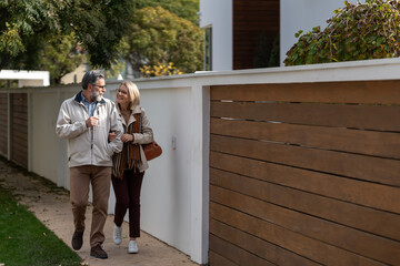 Smiling older couple walking arm in arm outdoors, enjoying a relaxed stroll in a pleasant residential neighborhood