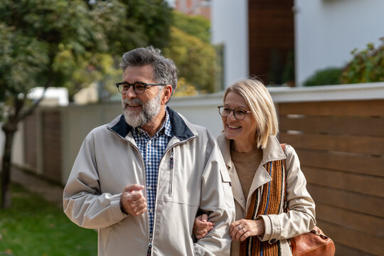 Smiling older couple walking arm in arm outdoors, enjoying a relaxed stroll in a pleasant residential neighborhood