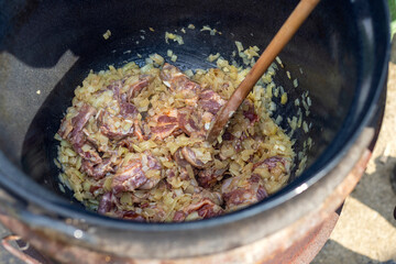 Stewed pork belly with onion with bones in a large pot with juice and sauce. Hot cooked meat. Cooking goulash in nature. Background