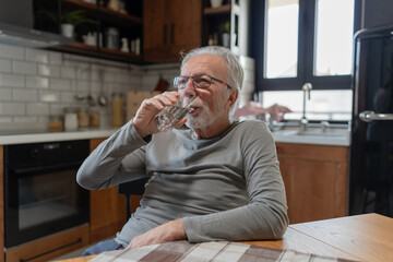 Elderly man drinking a glass of water while sitting in a modern kitchen, captured in a natural and relaxed moment