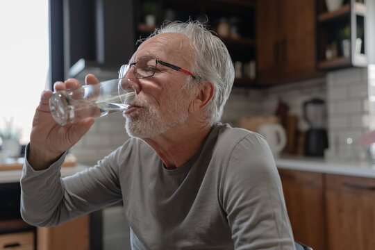 Elderly man drinking a glass of water at home, taking a moment to stay hydrated in a cozy kitchen setting
