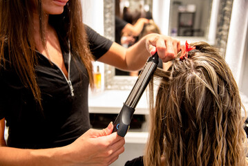 Hairdresser styling woman's wavy hair with curling iron