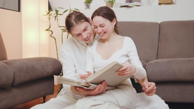 Young couple shares a moment while looking at a scrapbook together on the floor of their living room during the afternoon