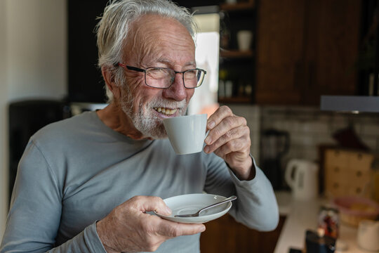 Elderly man sipping hot coffee from a cup while standing in a cozy kitchen, enjoying a quiet morning moment