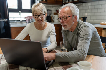 Senior couple using a laptop together at the kitchen table, focused on browsing or managing online tasks