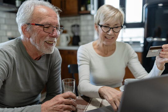 Senior couple using a laptop together at the kitchen table, focused on browsing or managing online tasks - Powered by Adobe