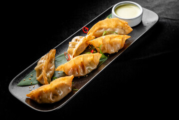Golden brown pan-fried gyoza dumplings on a dark slate plate with a side of dipping sauce and garnish against a black background