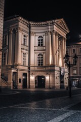 Fototapeta premium The historic Estates Theatre in Prague illuminated at night, showcasing its elegant neoclassical facade, ornate columns, and timeless architectural charm.
