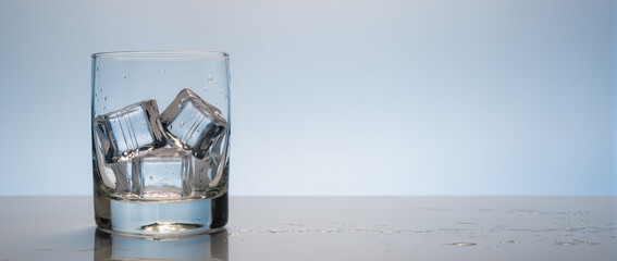 Ice cubes in glass on table with reflections and textured surface. Clear ice cubes in a glass creating refreshing ambiance on wooden surface. Concept of cocktails and beverages for social events.