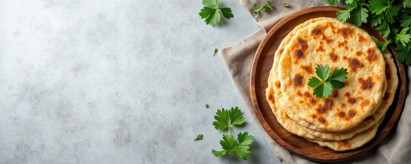 Indian chapati flatbreads on wooden plate with fresh parsley garnish. Food photo is top view with copy space. Traditional Indian cuisine concept. Baked wheat tortillas at gray table.
