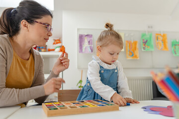 Fototapeta premium Caregiver and young girl working together on a colorful alphabet puzzle in a bright, playful classroom setting