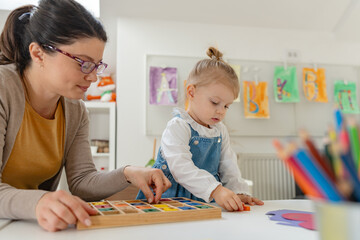 Fototapeta premium Caregiver and young girl working together on a colorful alphabet puzzle in a bright, playful classroom setting