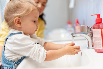 Toddler washing hands at a bathroom sink with a smiling parent nearby, promoting hygiene, cleanliness and health education at home. Family routine, child safety and disease prevention concept