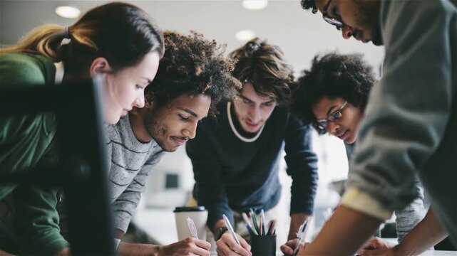 Diverse group of young adults collaborating closely over a shared task or document
