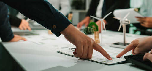 A dynamic meeting in a modern office, showcasing teamwork as individuals point at project plans focused on eco-friendly initiatives and renewable energy strategies. SACTR