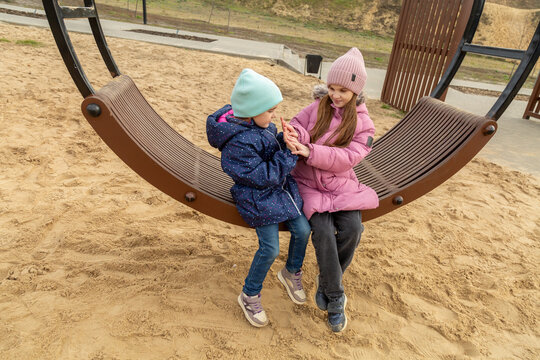 Children having fun on a swing on the playground in public park on autumn day. Happy child enjoy swinging. Active outdoors leisure for child in city - Powered by Adobe