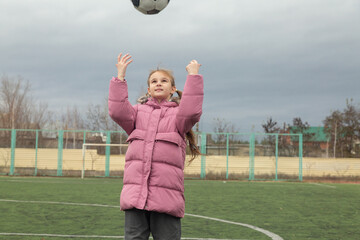 Little girl having fun playing a soccer/football game on autumn cloudy day. Active outdoors game/sport for children.