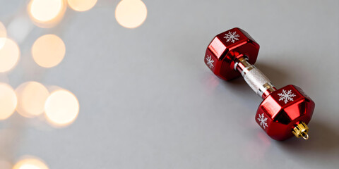 Bright red dumbbell ornament with snowflake patterns, lying on a neutral gray background with golden bokeh lights.