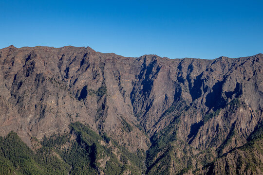 Primer plano de las escarpadas paredes y barrancos de la Caldera de Taburiente en La Palma, mostrando roca erosionada y vegetaci&oacute;n en las grietas bajo un cielo despejado.
