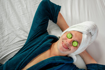Man with cucumber eye mask in bathrobe, having fun during skincare