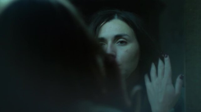 A distressed woman looks at her reflection, touching her face as if she no longer recognizes herself. A symbolic cinematic scene of dissociation, identity conflict, and emotional numbness. 