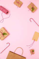 Gift wrapping supplies, decorations on pastel pink background. Craft boxes with red white twine, brown paper bag, candy canes, gift tag. Template for vertical posts, holiday content. Copy space