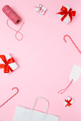 Gift wrapping supplies, Christmas decorations on pastel pink background. White gift boxes with red bows, candy canes, twine spool, paper bag, gift tag. Template for vertical posts, holiday content