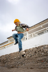 Happy little boy in yellow hat and casual clothes jumping down with raised arms, enjoying active play and freedom outdoors near the beach on a cloudy day