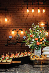 Buffet table in loft style: appetizers, berries and industrial lights against brick wall