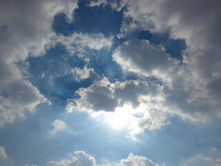Sunlight rays with bright clouds opening through blue sky creating a dramatic background