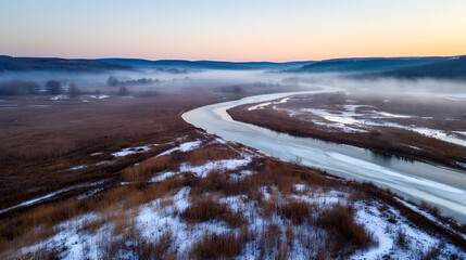 Aerial panoramic frozen river through snowy marsh at misty winter dawn