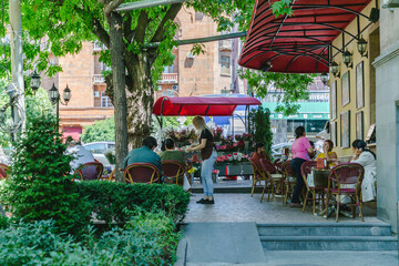 Yerevan, Armenia - 14 August 2025: View of a vibrant outdoor cafe scene, where the red awnings contrast with the lush green foliage and the bustle of Yerevan's urban life.