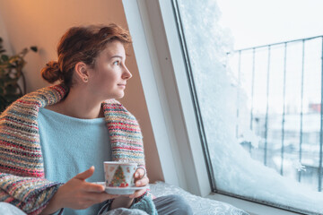 young woman warms up with hot tea in winter weather at home