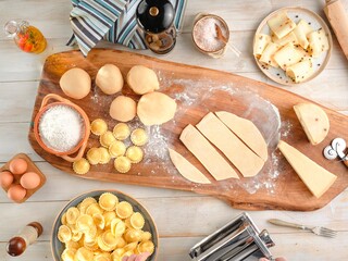 On a wooden board, pasta making is in full swing. Dough, flour, eggs, completed Girasoli and Pasta Machine, salt, and cheese are all placed together as the dish is being made